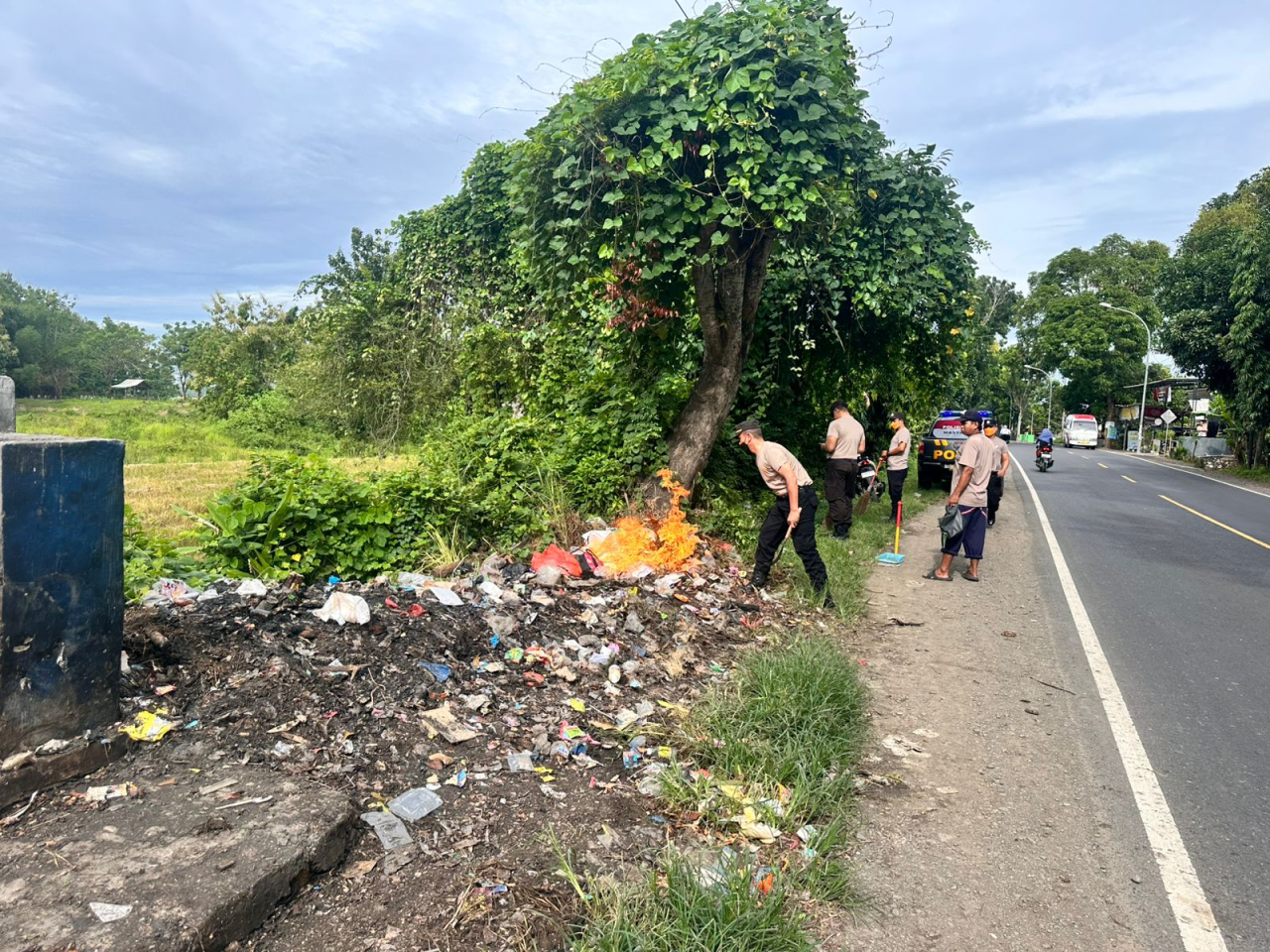 ‎Kapolsek Jrengik AKP Sunarno, SH bersama anggota saat membersihkan dan membakar tumpukan sampah di bahu jalan nasional yang melintasi Desa Jrengik, Kabupaten Sampang, Kamis (26/2/2026) pagi/Bn.